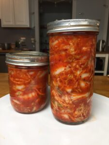 Two jars of prepared kimchi, or Korean pickled cabbage, one tall, one short.