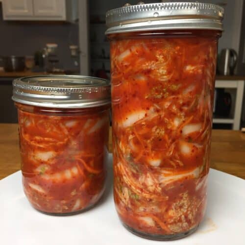 Two jars of prepared kimchi, or Korean pickled cabbage, one tall, one short.