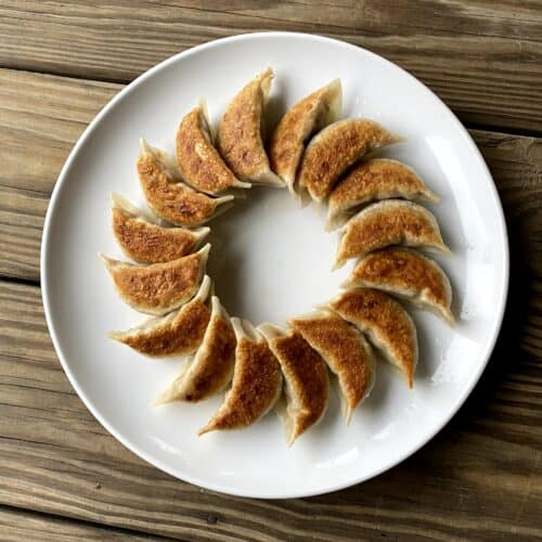 Pan fried dumplings in a circle on a white plate.