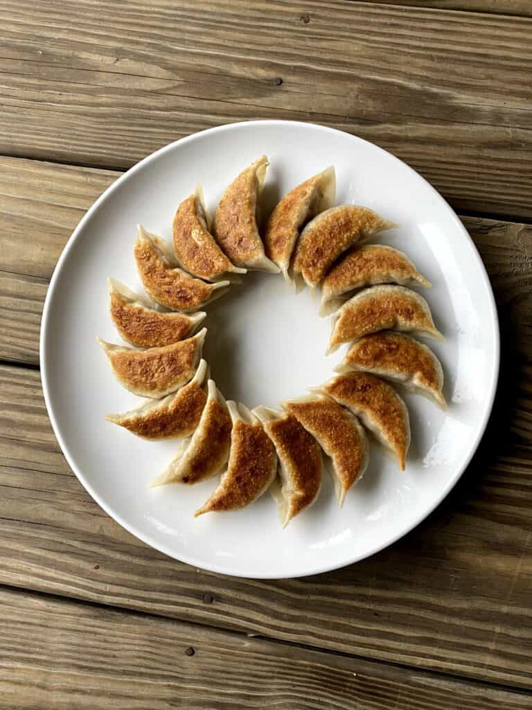 Pan fried dumplings in a circle on a white plate.