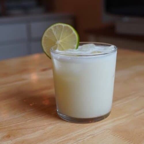 White frothy lemonade in a rocks glass with lime wedge on edge of glass.