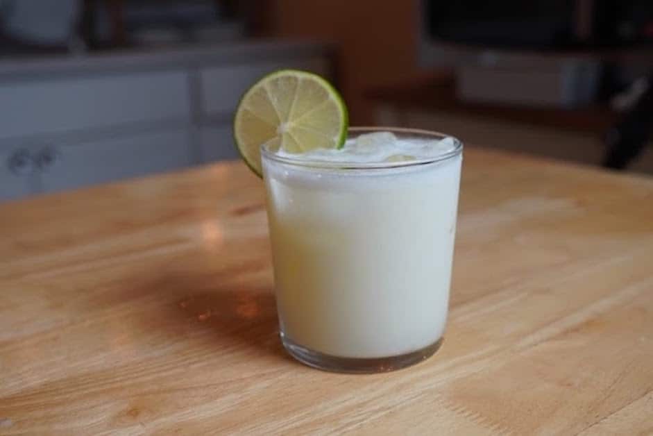 White frothy lemonade in a rocks glass with lime wedge on edge of glass.