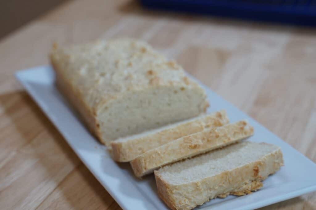 Loaf of rice bread on white serving plate. Three slices have been cut, revealing the inner texture of the bread.