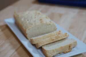 Loaf of rice bread on white serving plate. Three slices have been cut, revealing the inner texture of the bread.