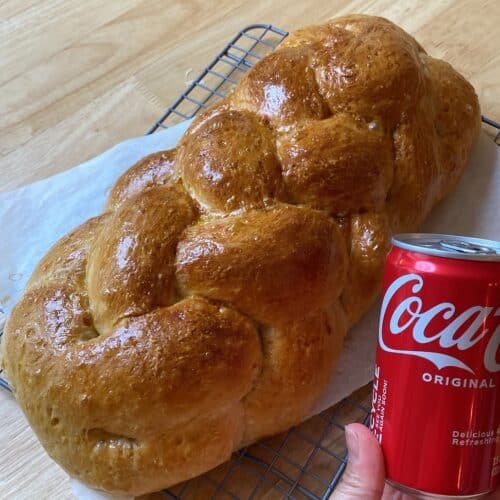 Hand holding small sized Coca-Cola next to a braided loaf of freshly backed bread.