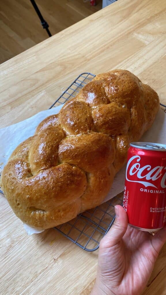 Hand holding small sized Coca-Cola next to a braided loaf of freshly backed bread.