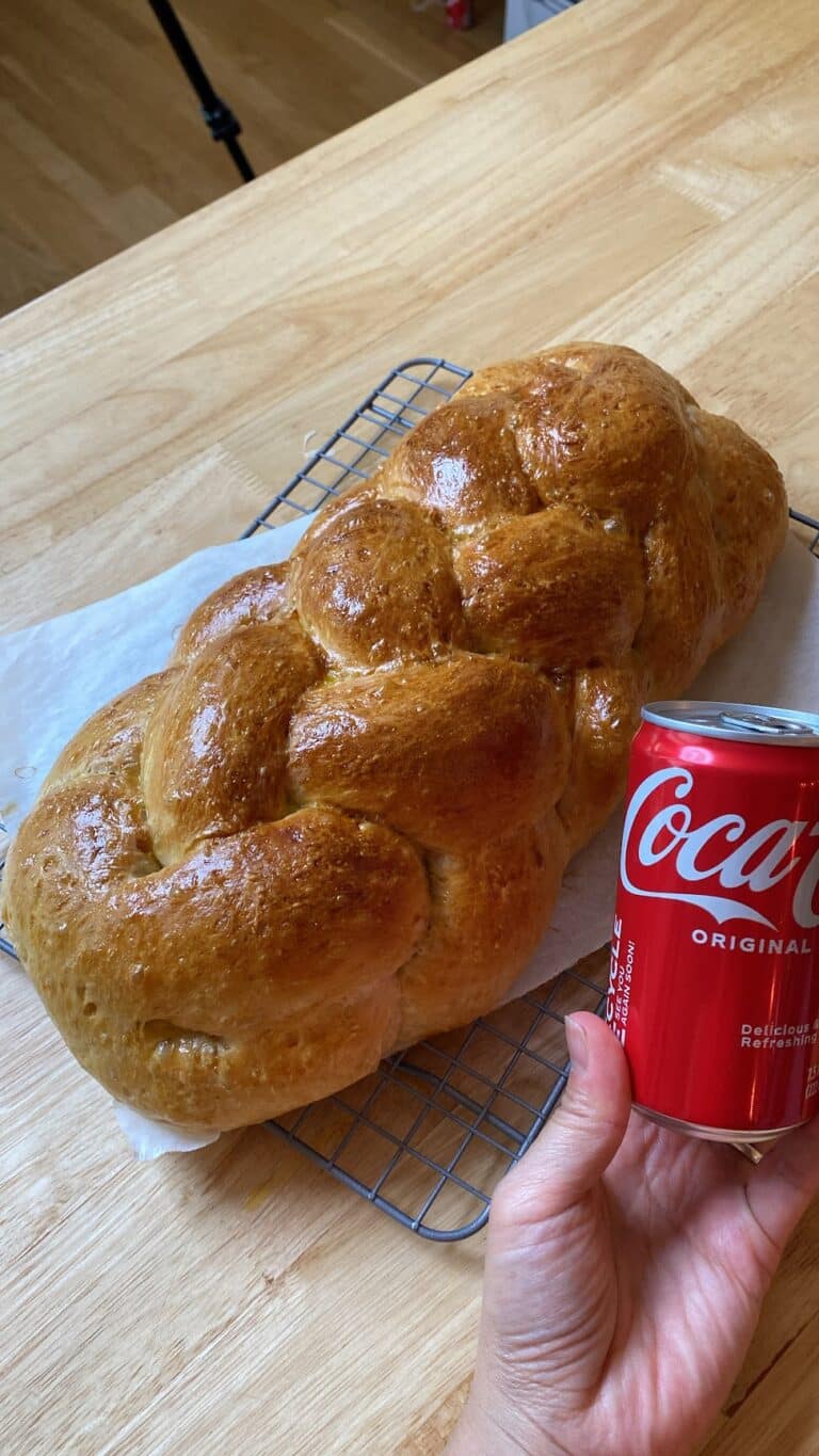 Hand holding small sized Coca-Cola next to a braided loaf of freshly backed bread.