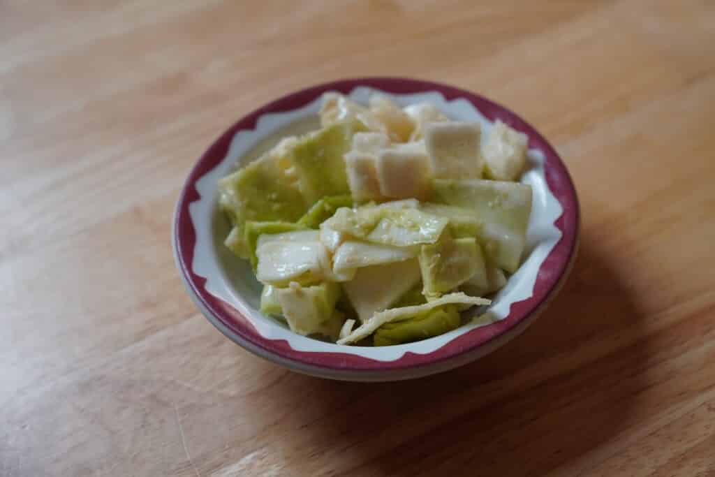 White ceramic bowl with brown edges holding a cabbage salad. Salad itself is light green, creamy looking, and chunky.
