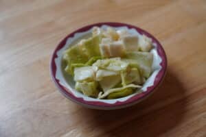 White ceramic bowl with brown edges holding a cabbage salad. Salad itself is light green, creamy looking, and chunky.