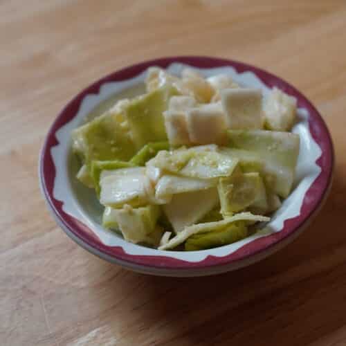 White ceramic bowl with brown edges holding a cabbage salad. Salad itself is light green, creamy looking, and chunky.