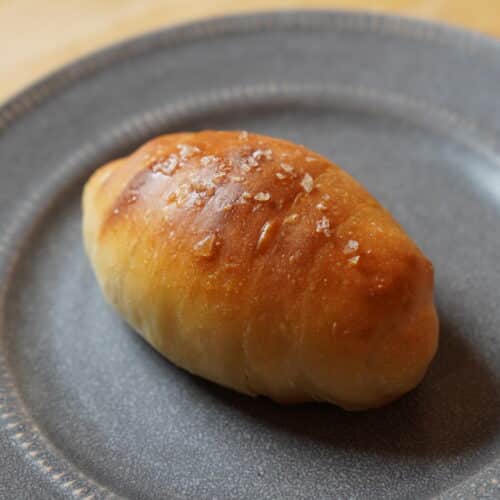 Salt flecked dinner roll on grey plate.