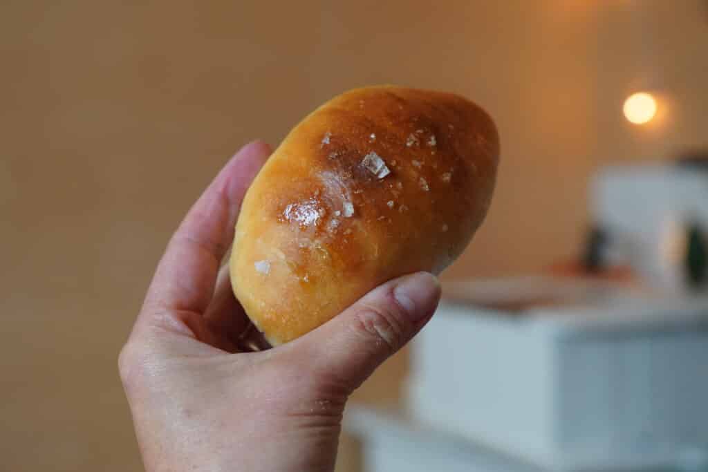 Hand holding crescent shaped chubby roll. Flakes of salt can be seen on the nicely browned top of the roll.