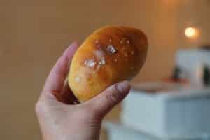Hand holding crescent shaped chubby roll. Flakes of salt can be seen on the nicely browned top of the roll.